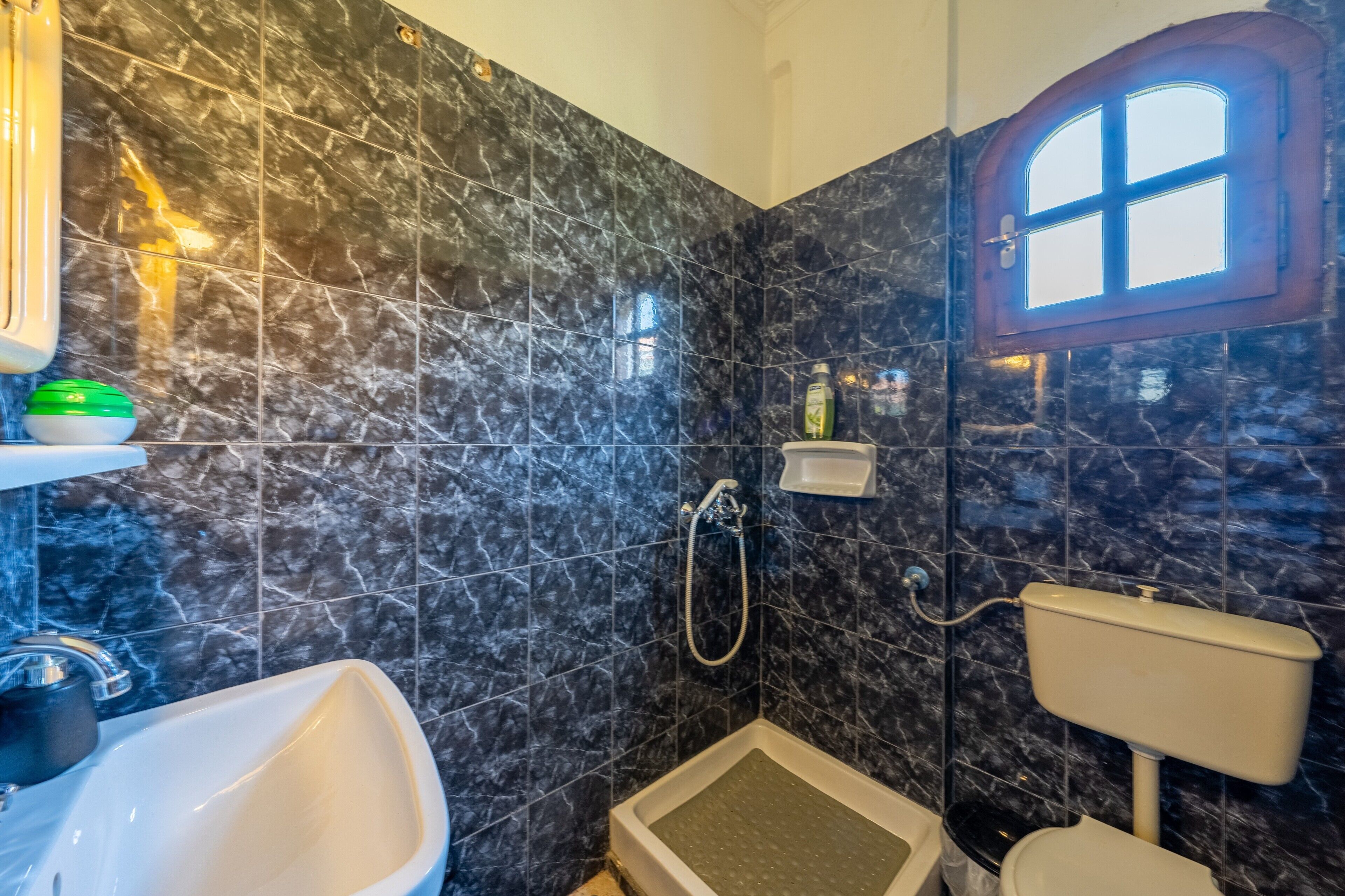 Une salle de bain comprenant des toilettes, un bidet et un lavabo, le tout adossé à un mur en marbre foncé.