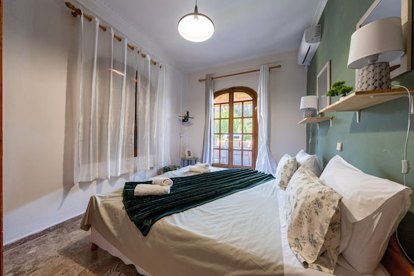 A bedroom with a bed, curtains, a window, a bedside table, and a lamp.