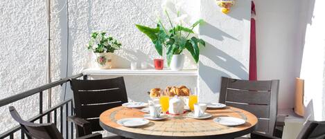 Una mesa redonda con sillas, una planta en maceta y un plato decorativo en un balcón con una pared blanca y texturizada.