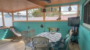 Zona de pati coberta amb cadires de vimet i una taula, un ventilador de sostre i un televisor penjat a la paret.