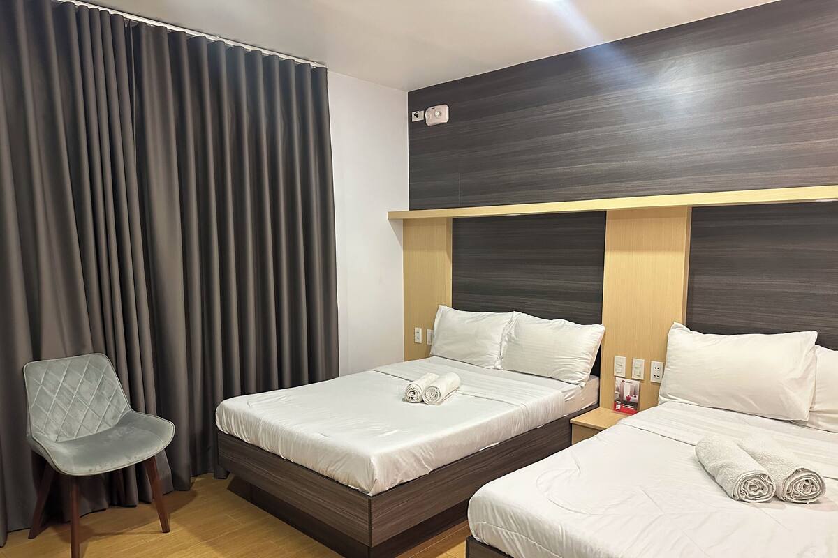 A hotel room with two beds, a chair, and a curtain.