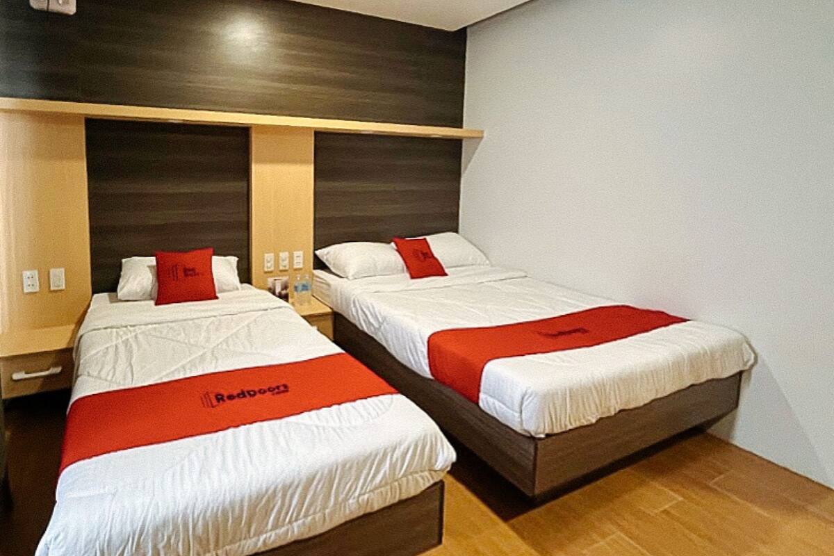 A hotel room with two beds, each with a red bedspread, wooden headboards, and a wooden floor.