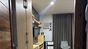 A compact living space with a kitchenette, a small seating area, and a wooden wardrobe. - Rudhil's Place Hotel (Cebu City)