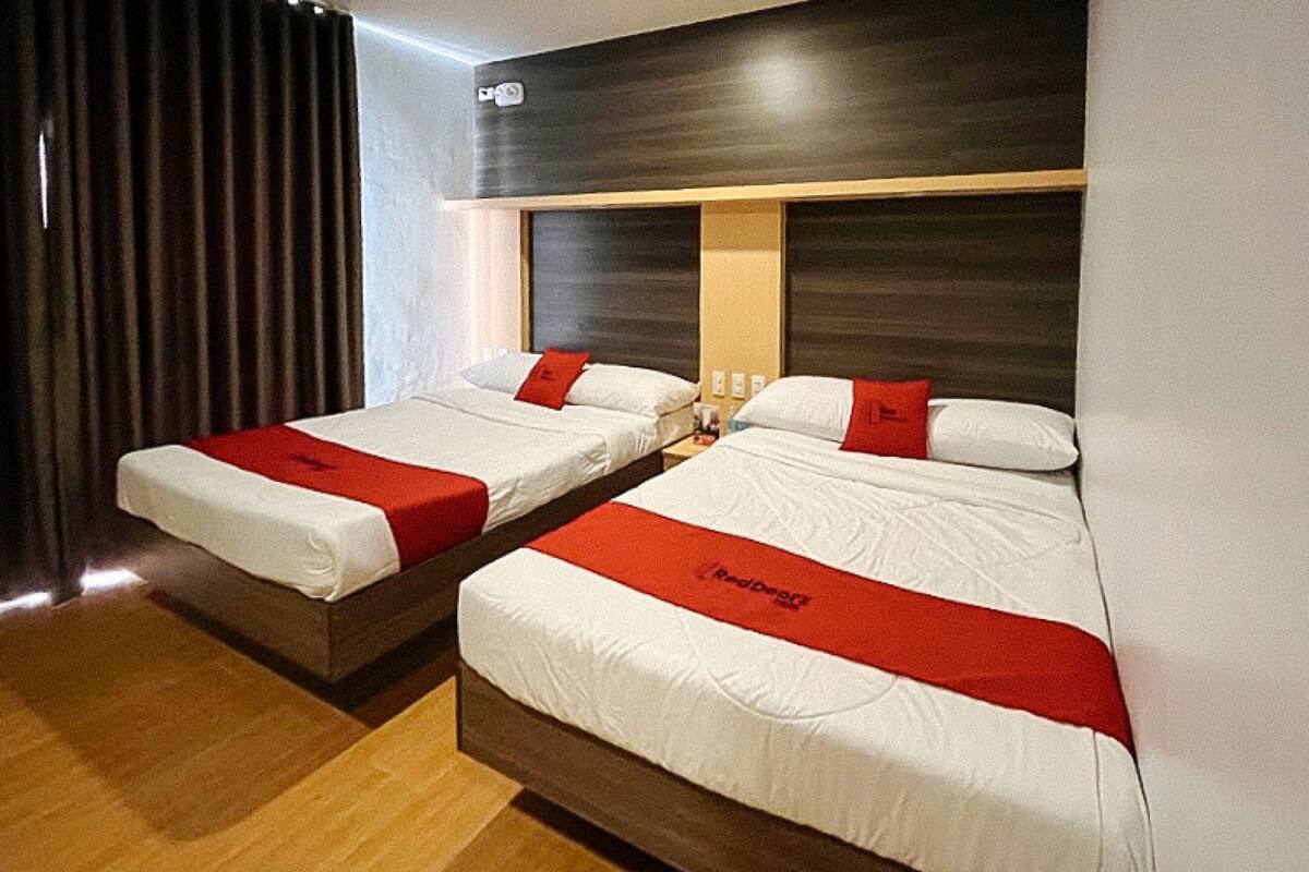 Two adjacent beds with red bedspreads, wooden headboards, and a dark wall.