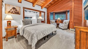 A cozy bedroom with a large bed, wooden ceiling beams, a chair, and a painting on the wall. - Big Foot’s Den on the 10/Northstar Resort Truckee (Truckee)