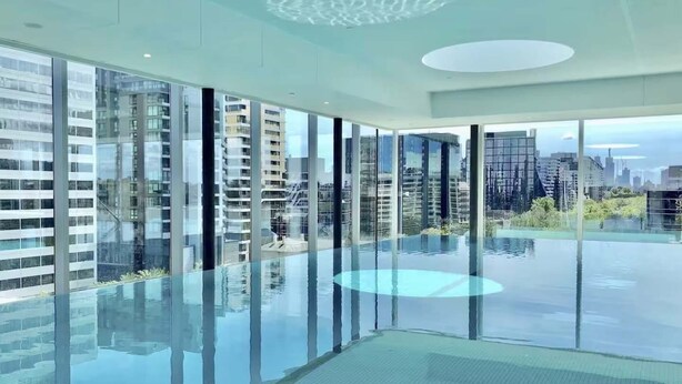 Piscina interior moderna con paredes de vidrio que ofrece vistas de rascacielos circundantes.