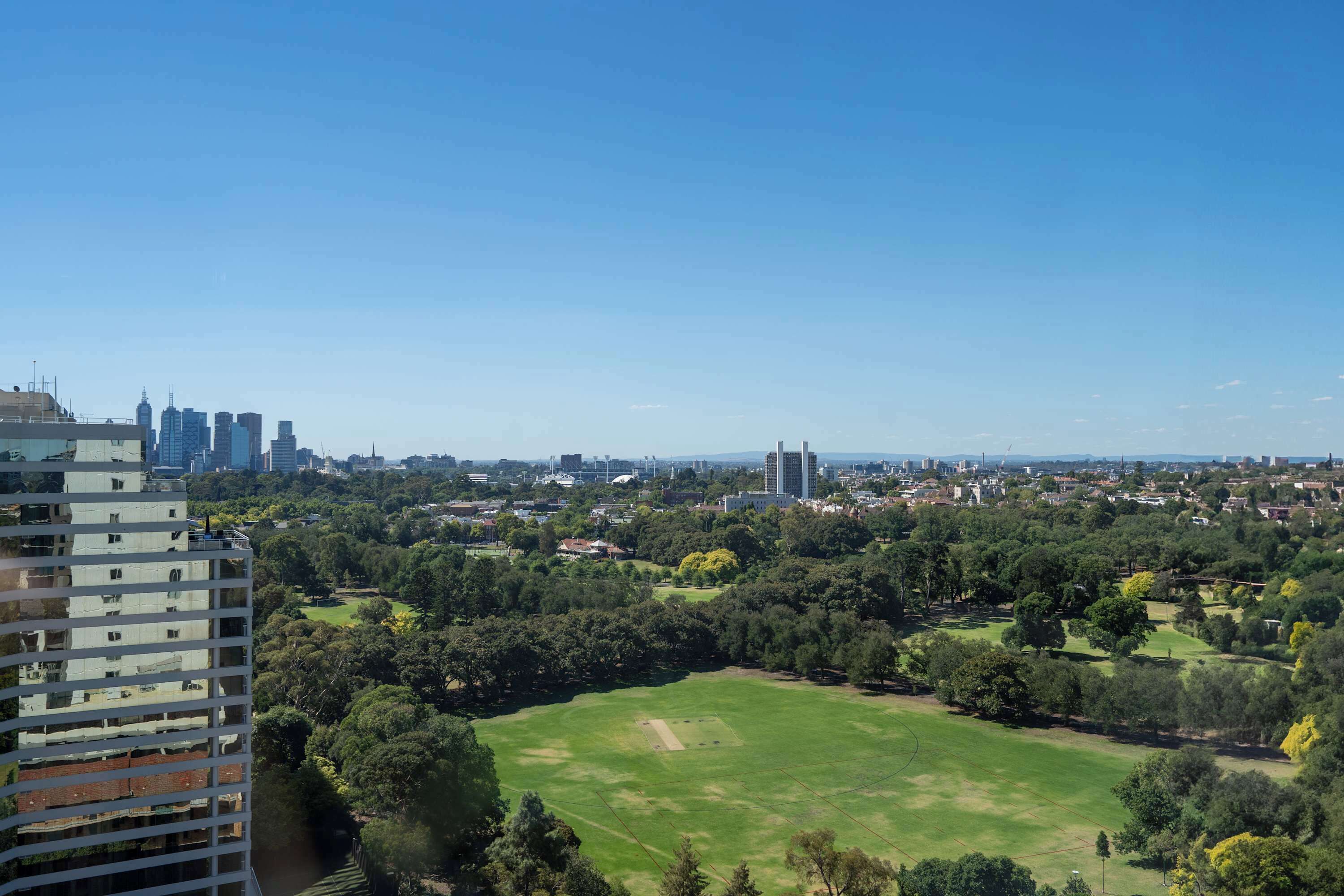 Un immeuble de grande hauteur, doté de nombreux étages et de balcons, qui donne sur un parc avec un vaste espace ouvert.