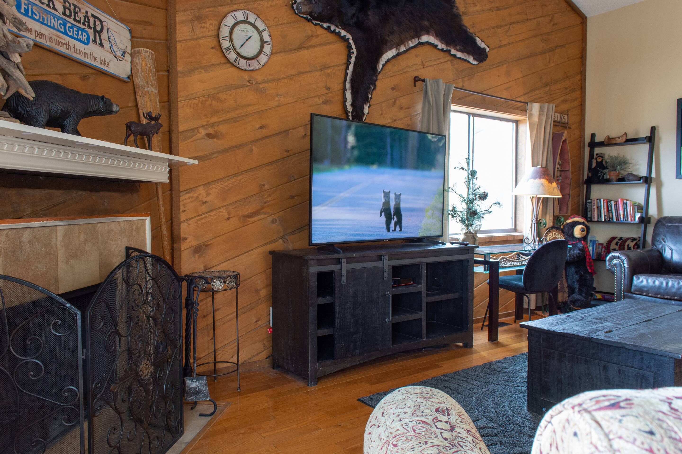 Un salon chaleureux avec une télévision, des murs en bois, une tête d’ours empaillée accrochée au mur et une bibliothèque.