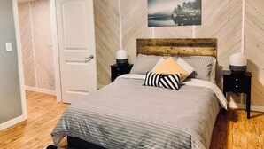 A bedroom with a bed, two bedside tables, a nightstand, a door, and a wall-mounted picture. - The Whispering Cedar (Valemount)