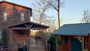 Eine Blockhütte mit Veranda, ein Auto davor und ein kleines Nebengebäude.