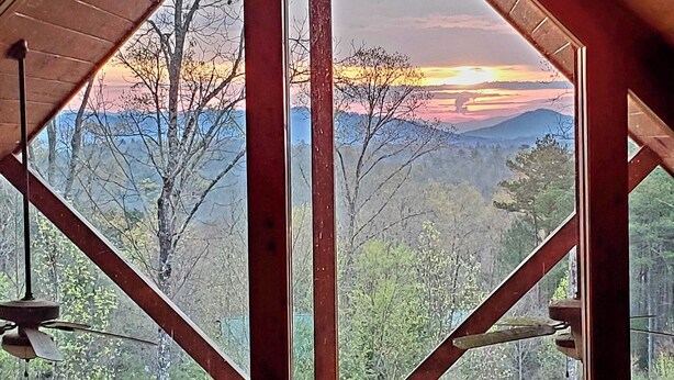 Ein Zimmer mit einer hohen Holzbalkendecke und Blick auf einen Sonnenuntergang über einer Berglandschaft.