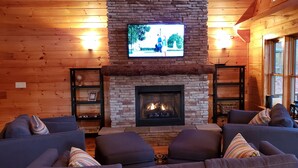 Ein gemütliches Blockhaus-Interieur mit Kamin aus Stein, einem an der Wand befestigten Fernseher und bequemen Sitzgelegenheiten.