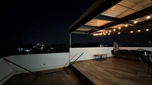Een terras buiten met houten vloer, lichtslingers en tuinmeubels.