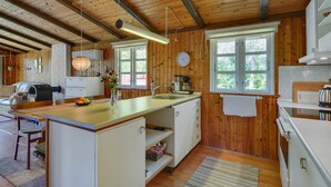 Et hyggeligt, landlig køkken i bjælkehytte-stil med trævægge, en stor ø-vogn og et spiseområde med sofa og bord.