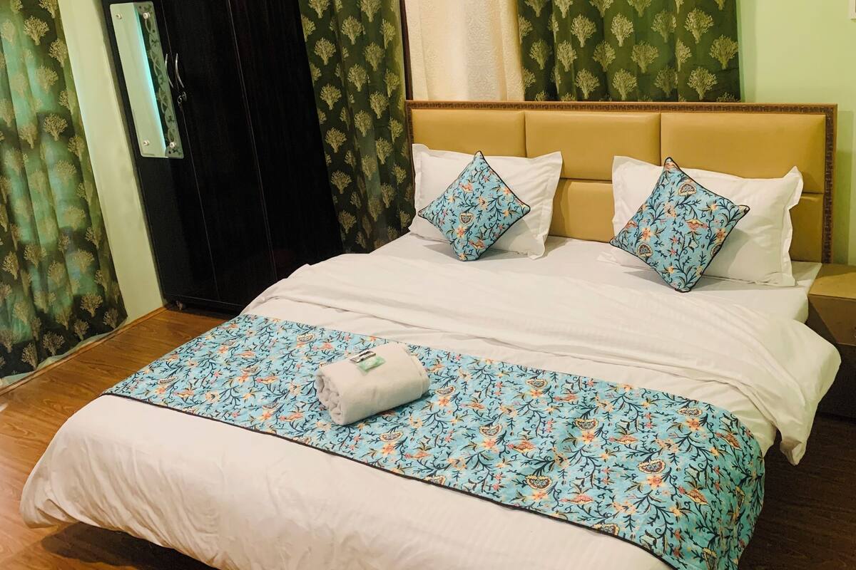 A double bed with white linens, two floral-patterned pillows, and a blue floral-patterned throw blanket.
