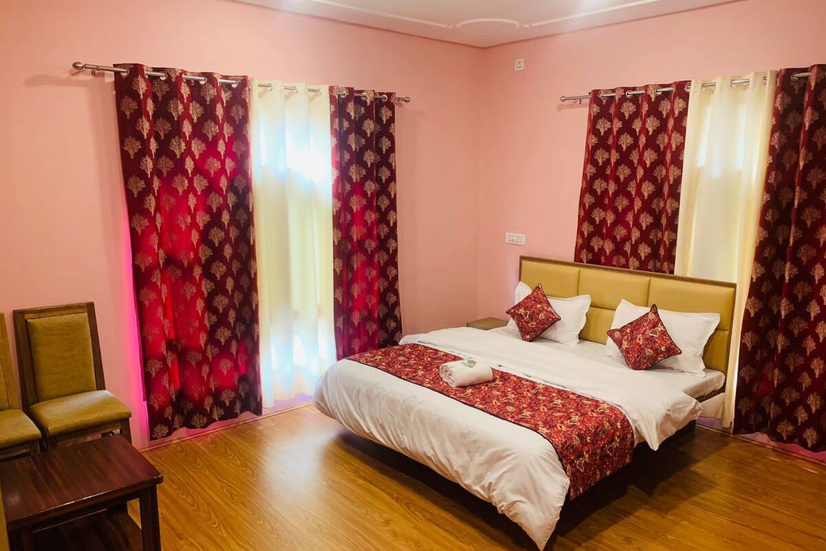 A hotel room with a large bed, two chairs, a small table, and patterned curtains.