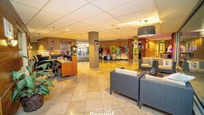 Un vestíbulo de hotel con mostrador de recepción, zona de estar y una gran planta en maceta.