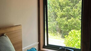 Un dormitorio con cabecera de madera, cama individual con ropa de cama color verde azulado y ventana con vistas a zonas verdes.