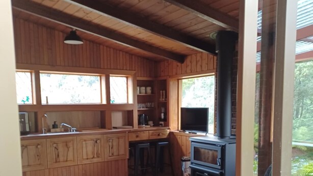 Un interior acogedor de cabaña con detalles de madera, una zona de cocina y un espacio de descanso con sofá y mesa.