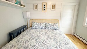 A bedroom with a bed, a bedside table, a lamp, and wall decorations. - Hotel-Style Suite, 300’ to Beach (Beach Haven)