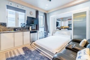 Quarto de hotel moderno com cama, sofá de couro, área de refeições e cozinha.
