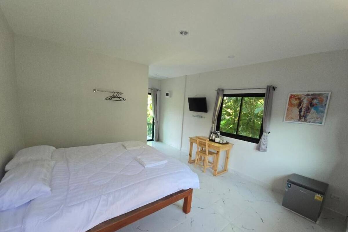 A bedroom with a bed, a small table, a TV, and a window.