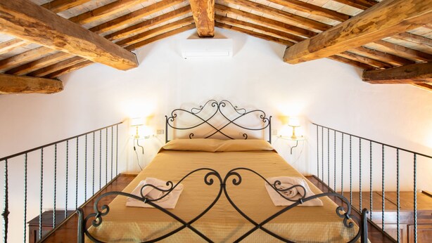 Een slaapkamer met een houten plafond, een bed met metalen frame en twee wandlampen.