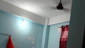 A small, single-room hotel room with two beds, a red curtain, and a ceiling fan.