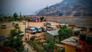 A parking area with several vehicles, a small building, and a road leading to a hilly landscape.