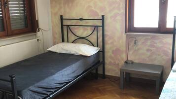 A single bed with a metal frame, a small bedside table, and a window with wooden blinds.
