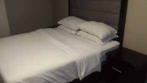 Una cama bien tendida con sábanas y almohadillas blancas en una habitación con cabecera oscura.
