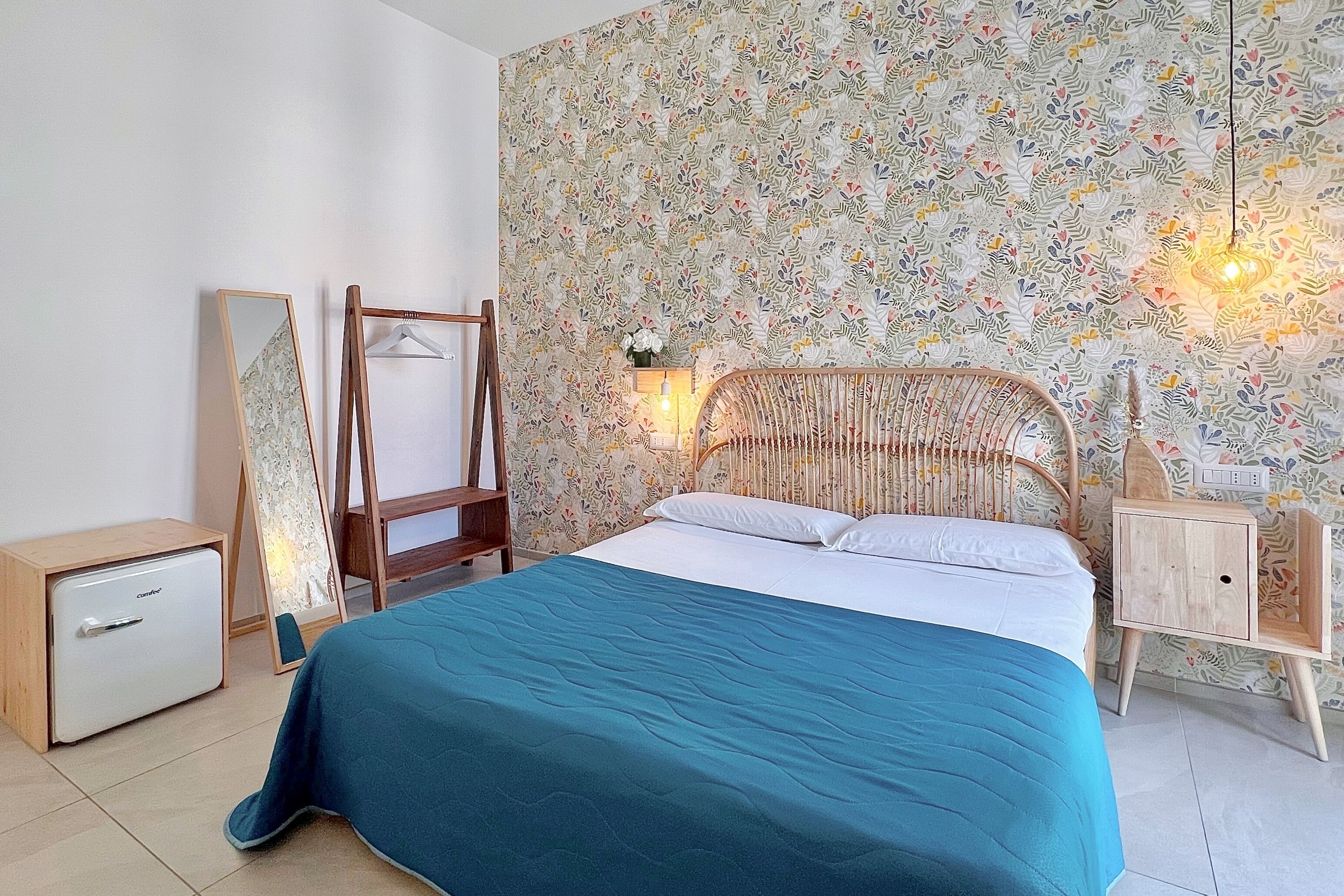 A bedroom with a bed, a wardrobe, a mirror, a hanging rack, and a wall-mounted light fixture.