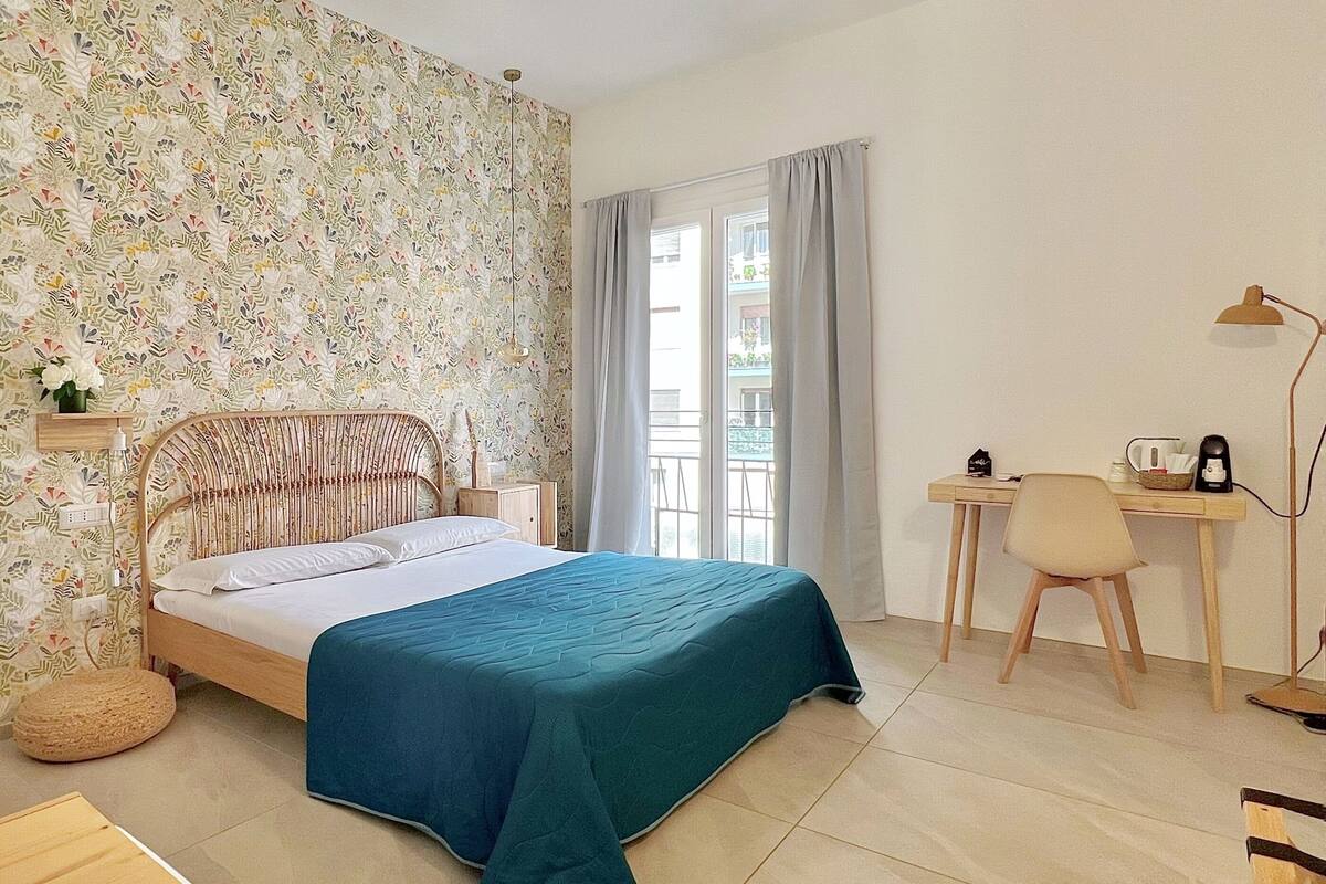 A bedroom with a bed, a desk, a chair, a lamp, and a window with curtains.