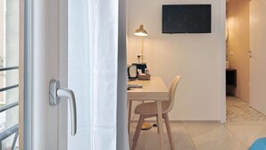 Una stanza con una porta, un tavolo con sedie, una lampada, una TV a schermo piatto fissata al muro e un pavimento a motivi.