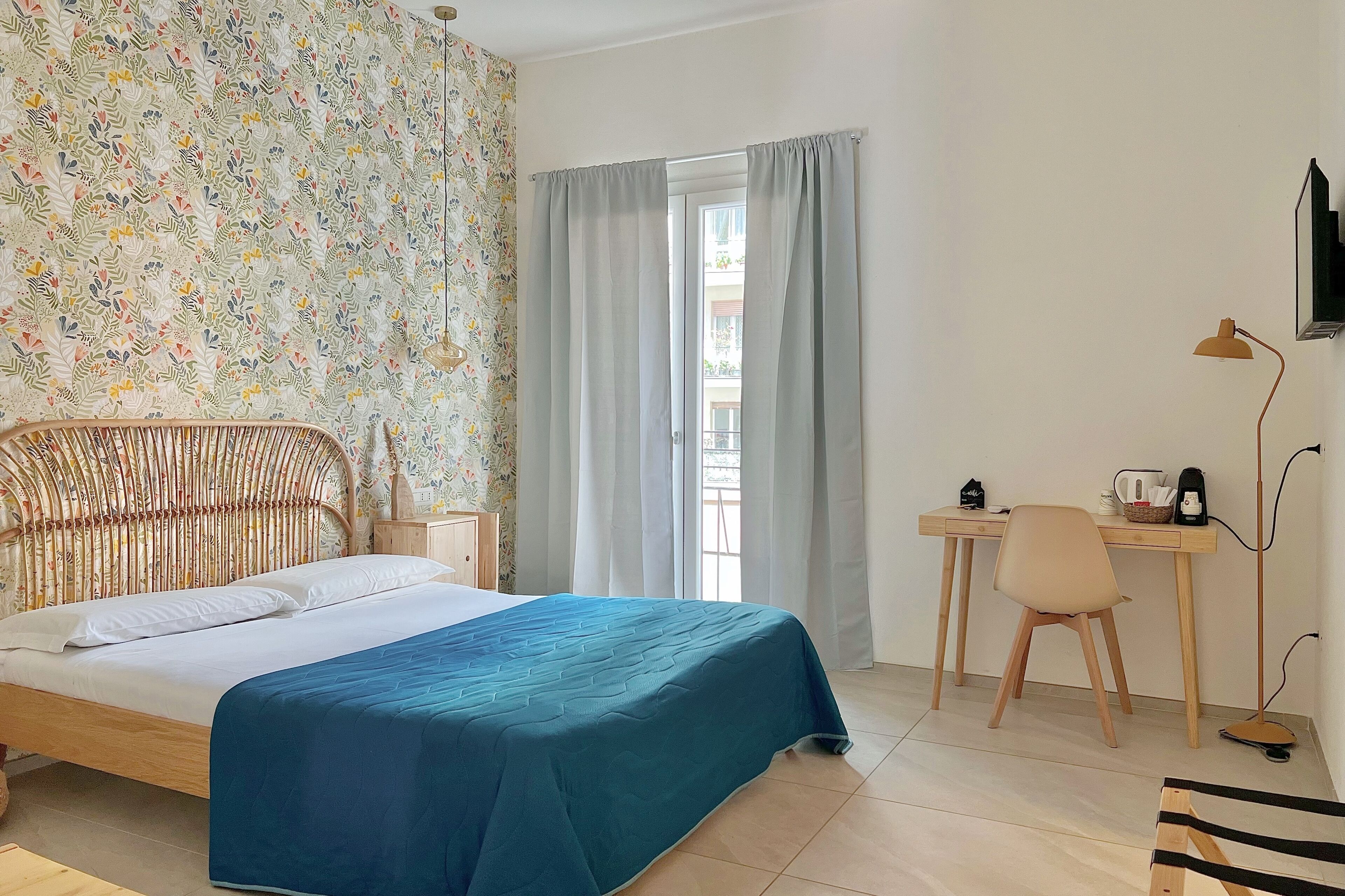 A room with a bed, a desk, a chair, a lamp, and a window with curtains.