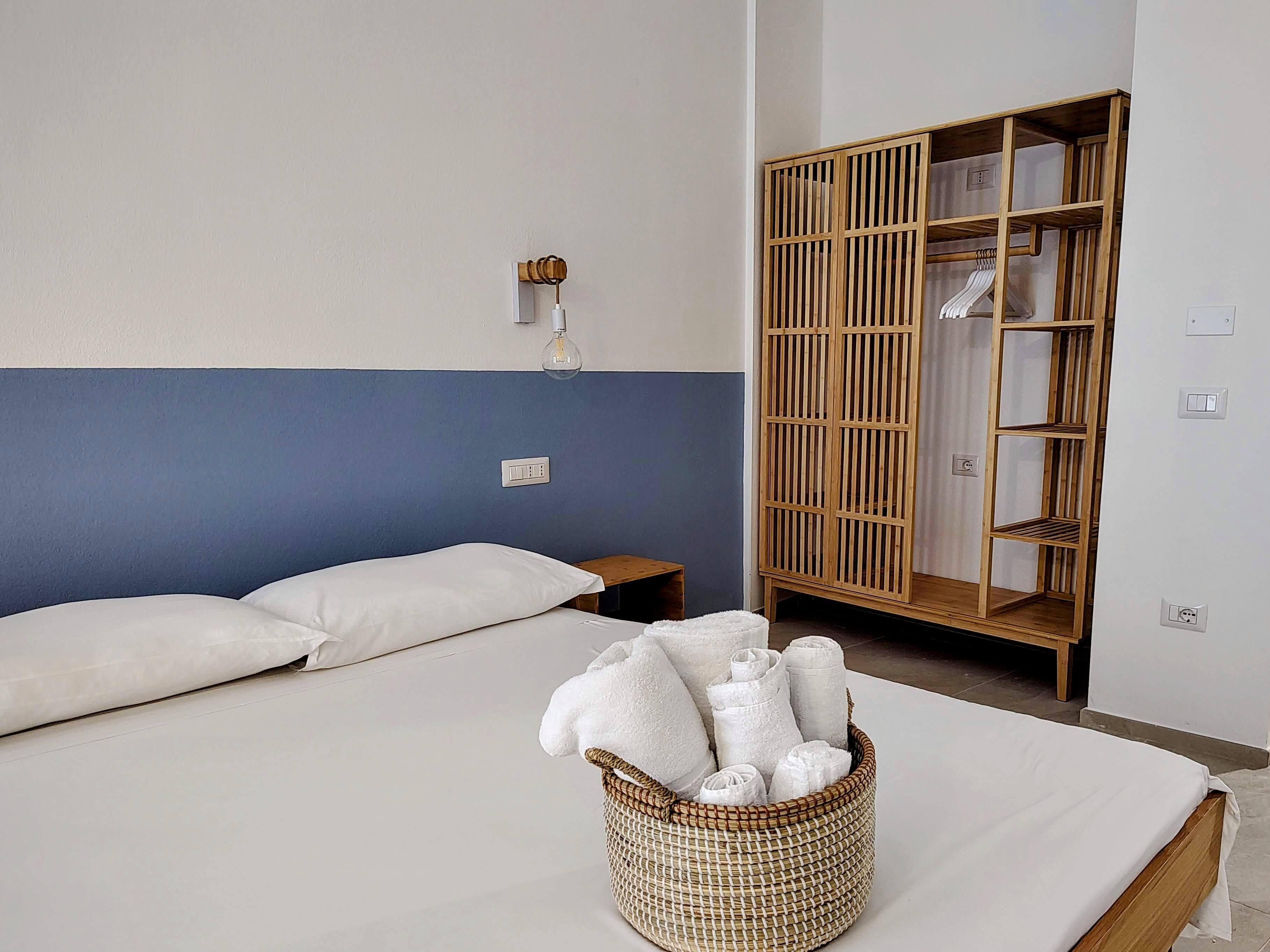 Un dormitorio con cama, mesita de noche, lámpara de pared, armario de madera y cesta de toallas.