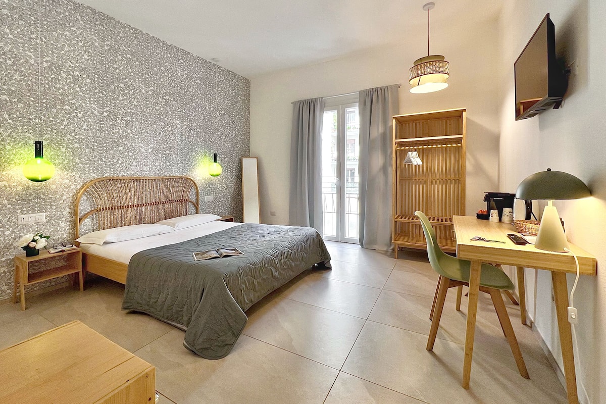 A bedroom with a bed, bedside tables, a desk, a chair, a wardrobe, and a television.