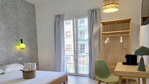 Una camera d'albergo con un letto, una scrivania, una sedia, una lampada e una finestra con tende.