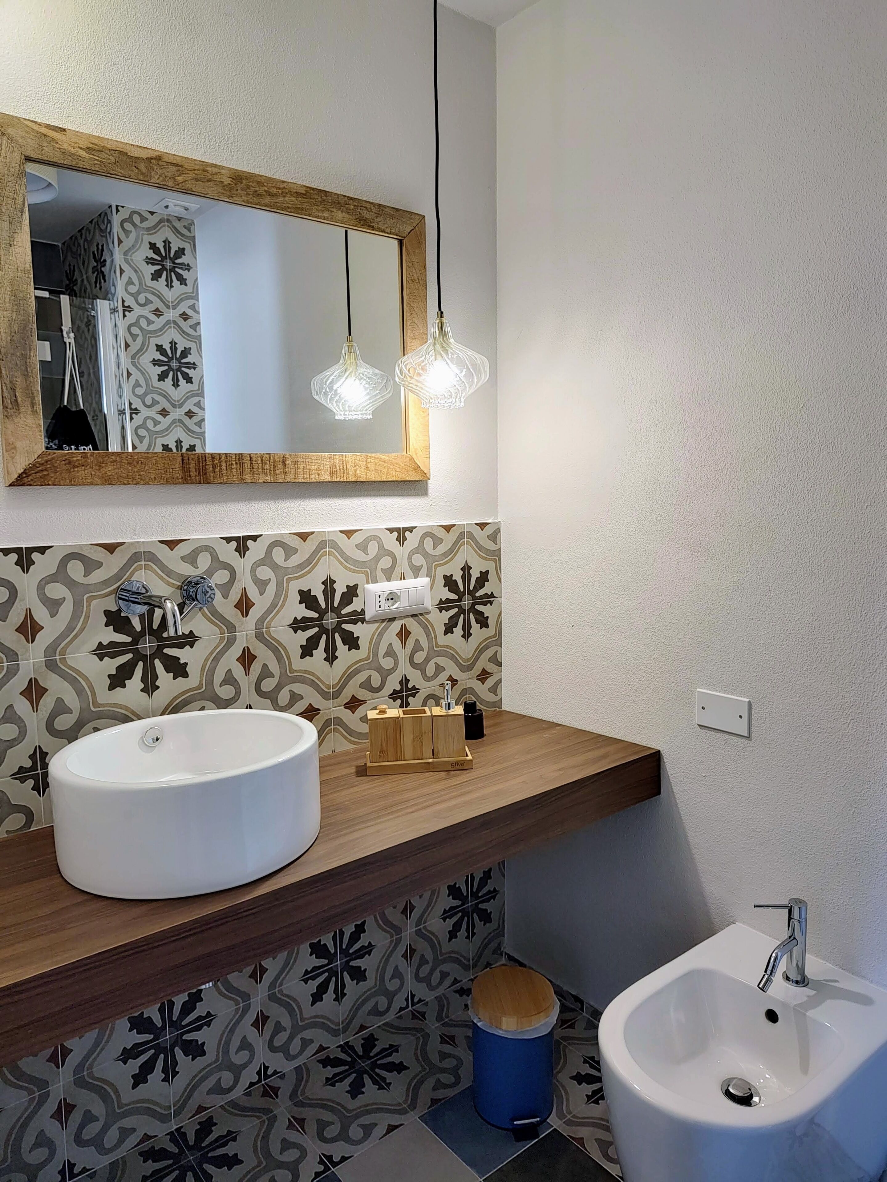 A bathroom with a large white sink, a smaller sink, a mirror with a wooden frame, and patterned tiles on the walls.