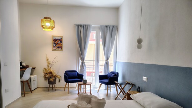 Una camera d'albergo con un letto, due poltrone, un tavolino, una lampada, un quadro appeso e una finestra con tende.