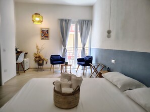 A hotel room with a bed, two chairs, a small table, a lamp, a picture on the wall, and a window with curtains. - La Casa di ViBi (Cagliari)