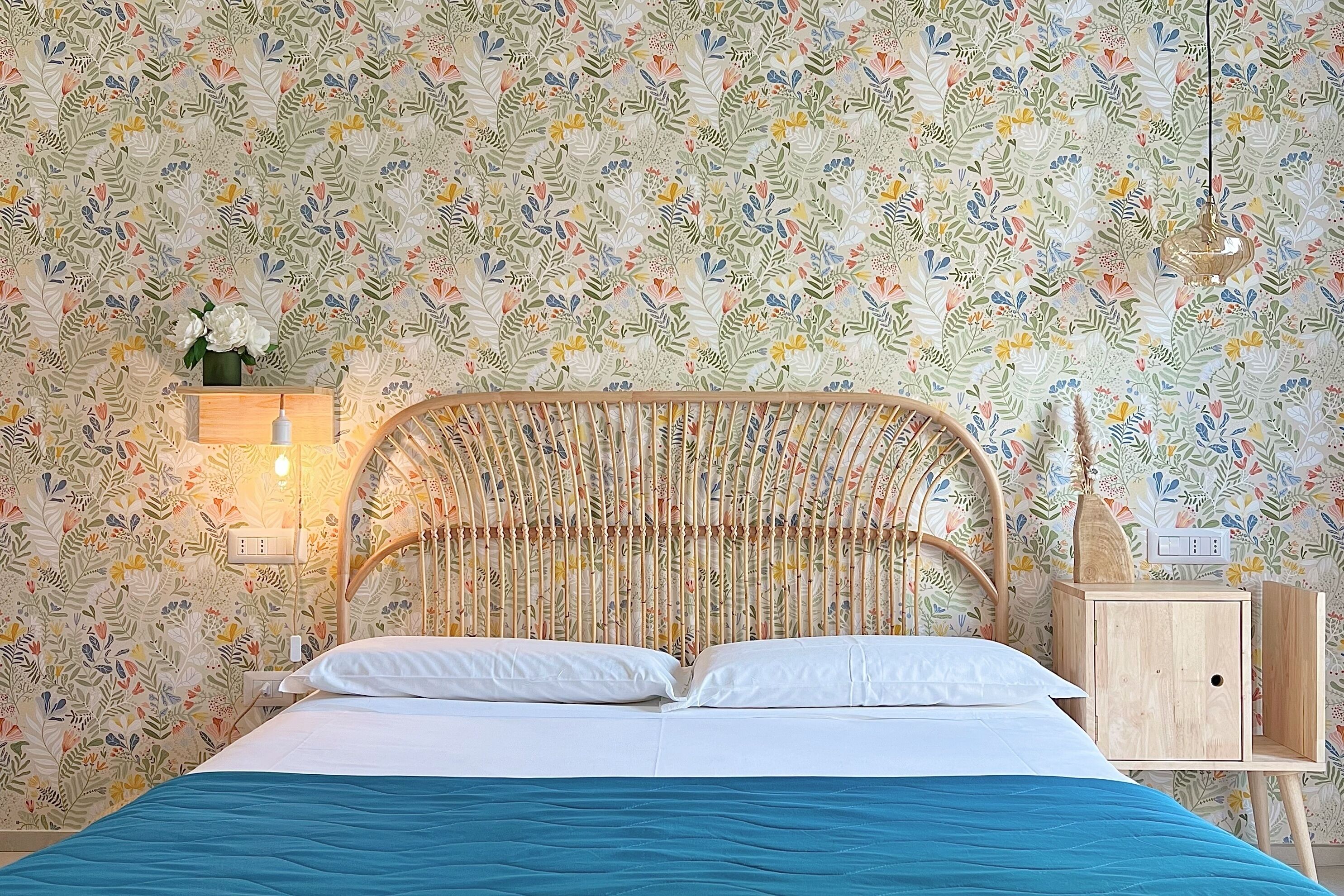 A bed with a blue bedspread, a wooden headboard, and a nightstand with a vase of flowers.