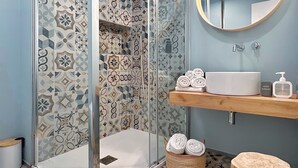 Un bagno con doccia, lavandino, specchio e uno sgabello.
