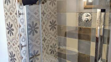 A modern bathroom with patterned tiles, a glass shower enclosure, and a visible hair towel.