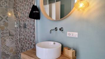 A bathroom with a white sink, wooden vanity, a mirror, and a geometric patterned shower wall.