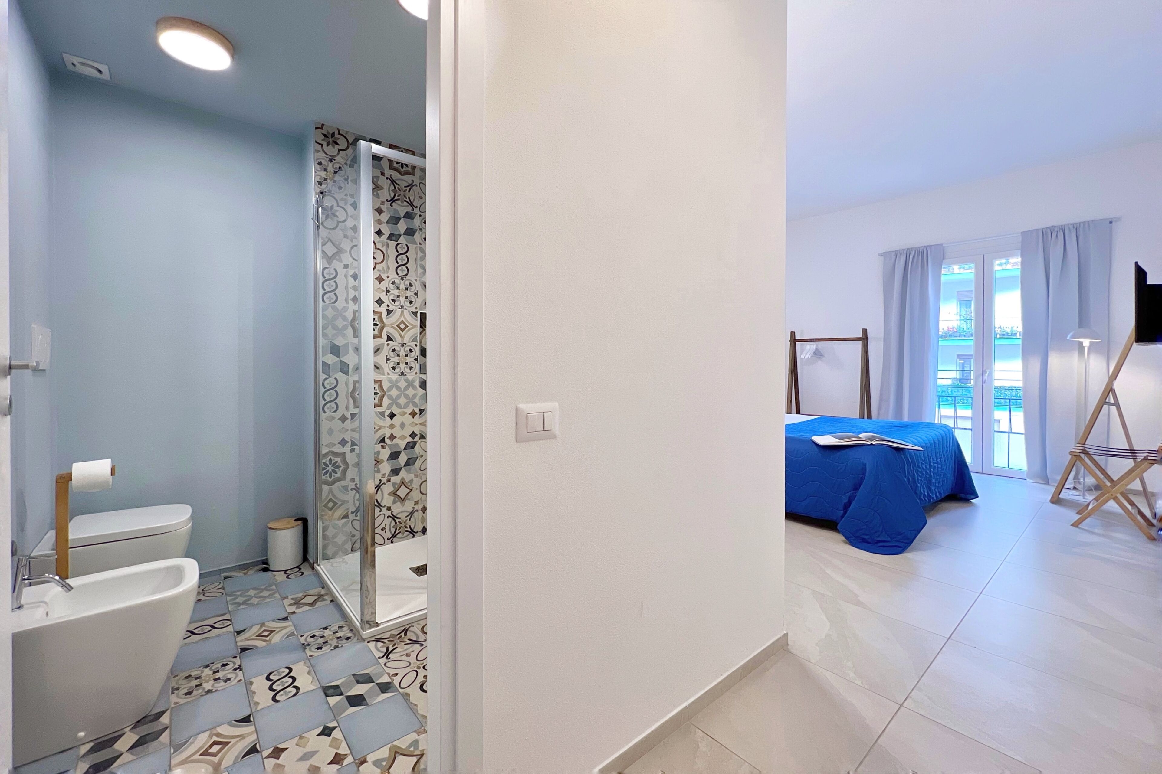 A bathroom with a toilet, bidet, and shower, and a bedroom with a bed and a TV.