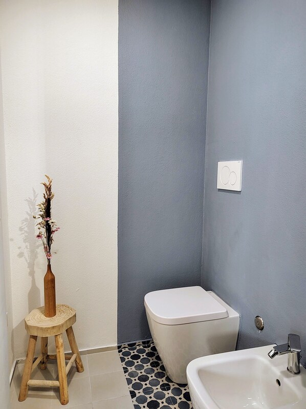 A bathroom with a toilet, sink, and a wooden stool with a vase of dried flowers. - La Casa di ViBi (Cagliari)