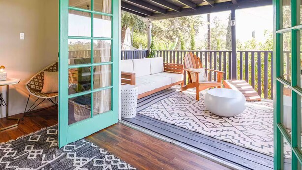 Un espacio exterior acogedor con terraza de madera, un sofá blanco y un otoman redondo blanco.