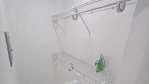 A bathroom with a white tiled floor, a shower area, and a shelf with a green bottle.