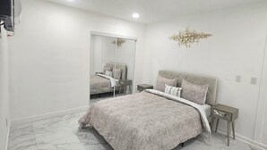 A bedroom with a large bed, a mirror, a chandelier, and a TV mounted on the wall.